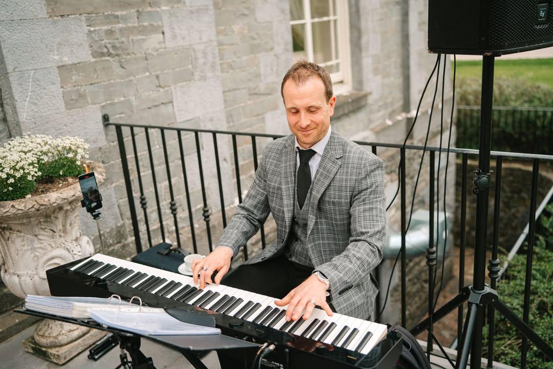 Joe Kenny pianist playing piano over a wedding drinks reception outdoors in Tankardstown House, Co. Meath